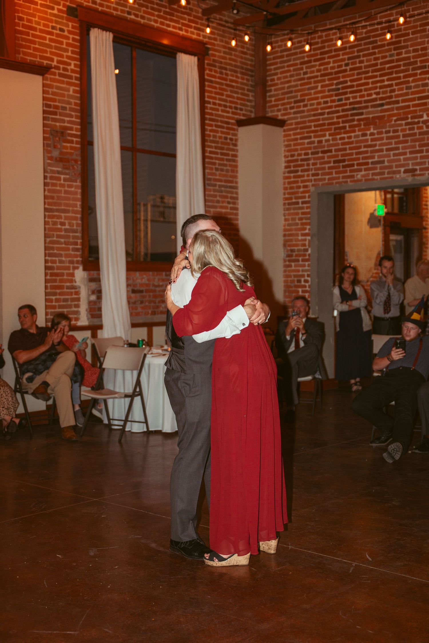 Couples dance together during a wedding reception in a warmly lit brick venue with string lights.