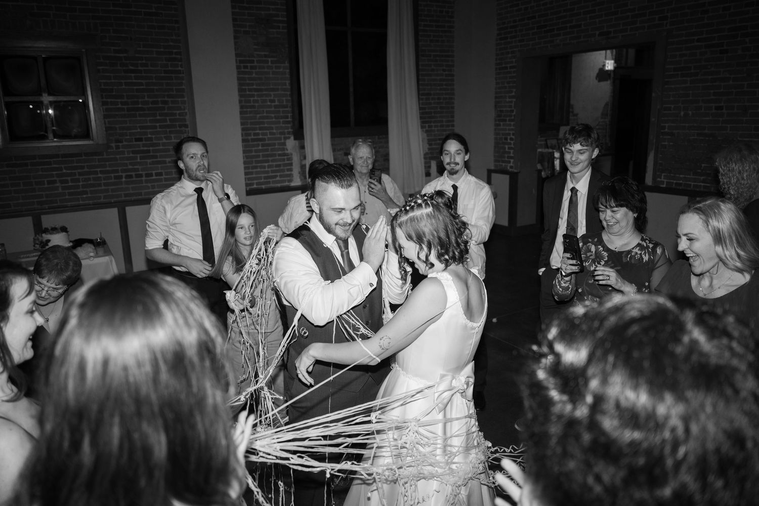 Wedding reception crowd gathered in dimly lit brick venue with string lights overhead.