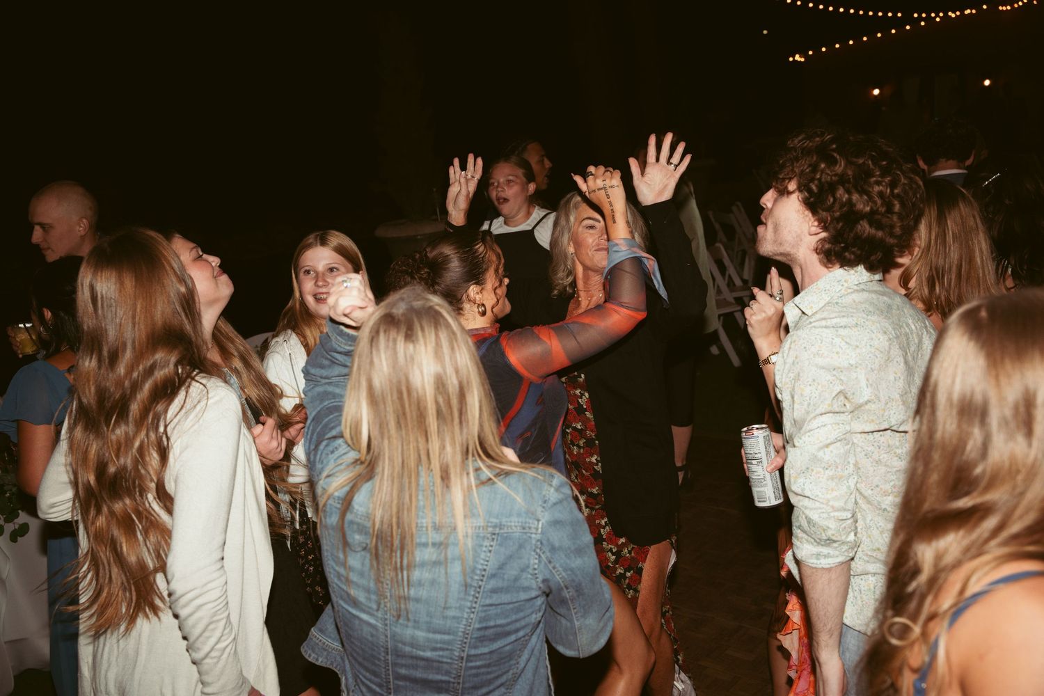 Guests dancing and celebrating under string lights at a nighttime wedding party.