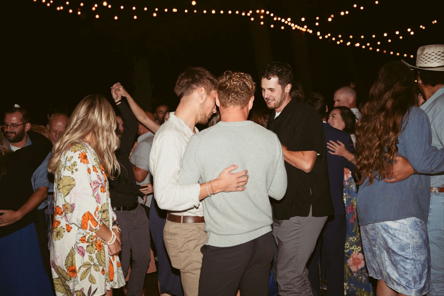 People dancing and embracing at a nighttime party under string lights.