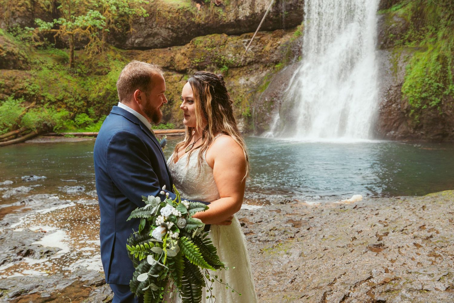 Romantic wedding portraits captured against the natural backdrop of a forest waterfall.