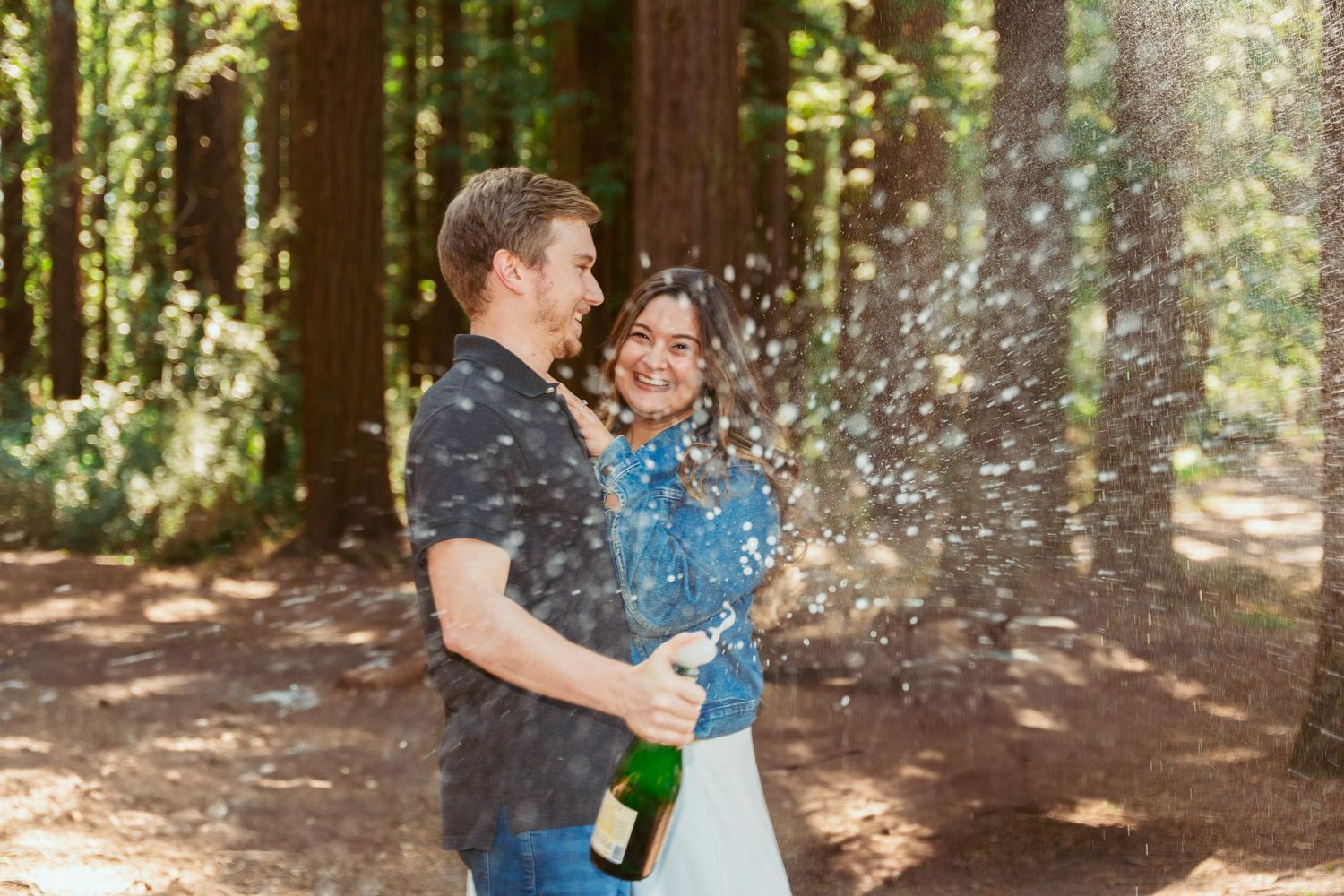 Playful champagne celebration moment in a wooded outdoor setting.