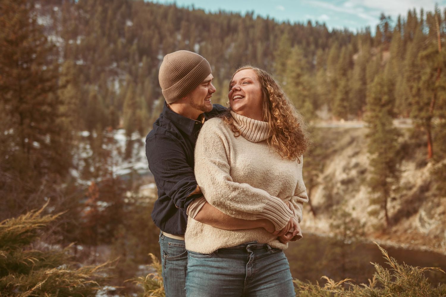 A couple shares a romantic moment against a mountainous winter landscape with evergreen trees.
