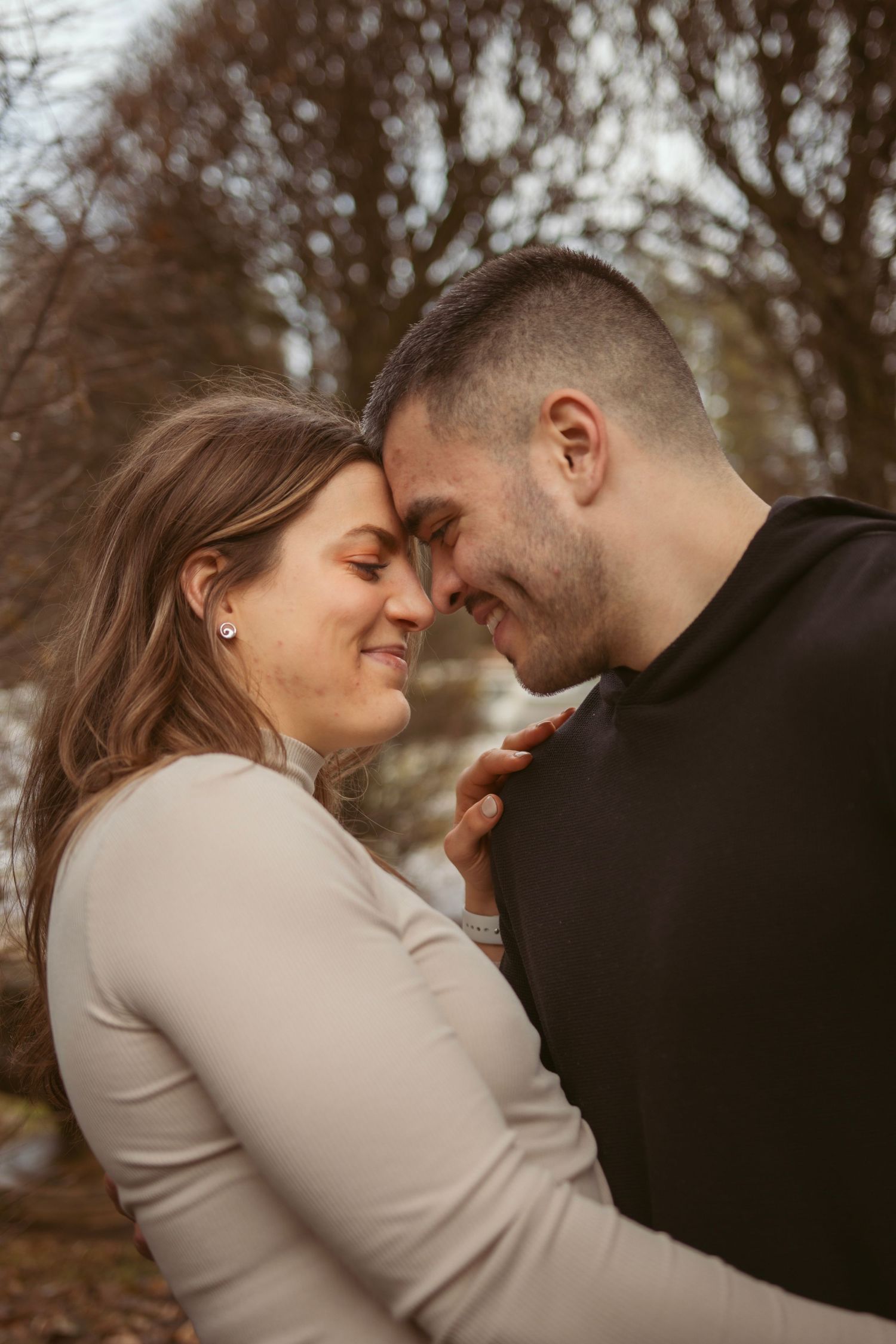 A couple in casual attire shares intimate moments outdoors on an autumn day.