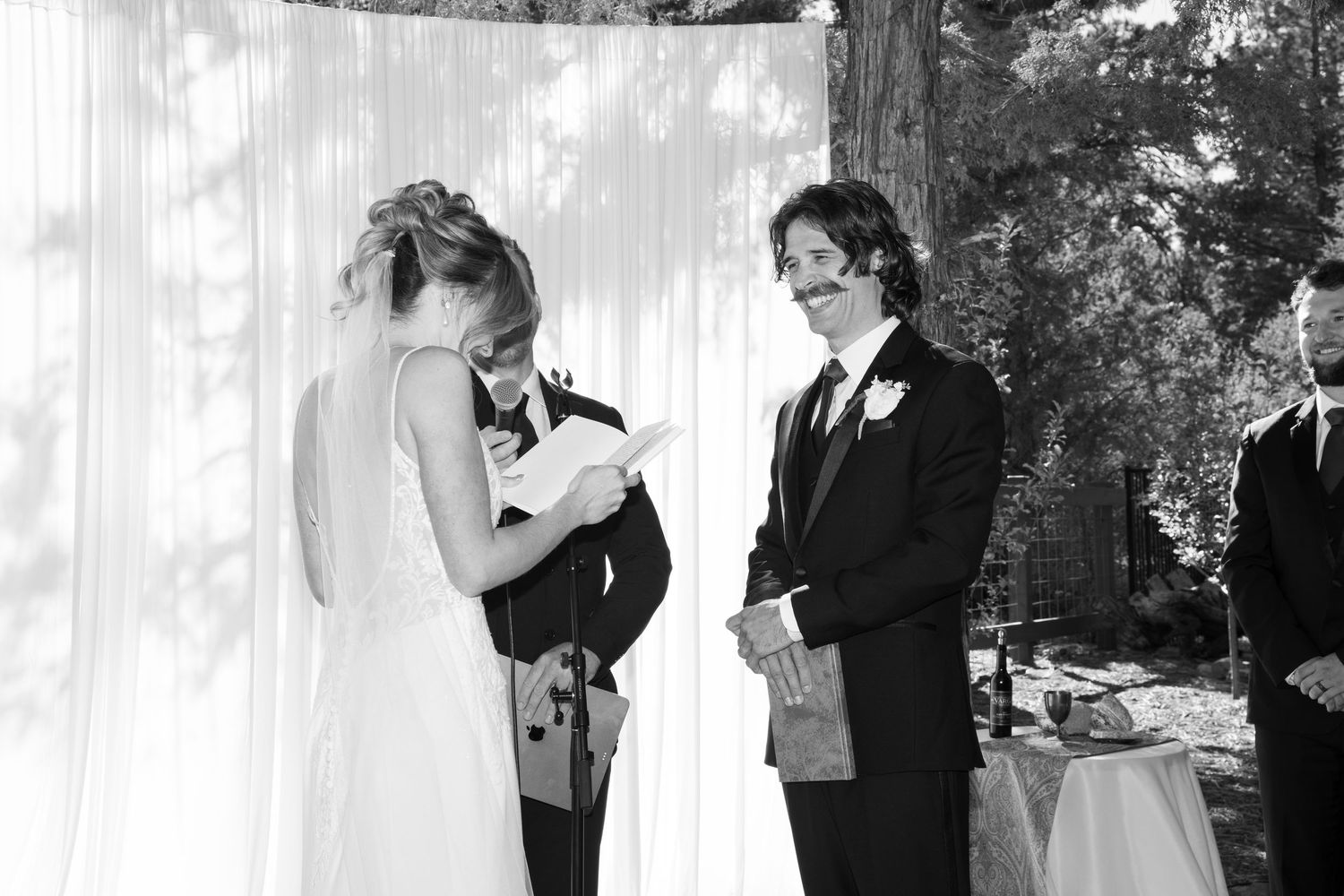 Wedding party stands beneath white draped fabric during a forest ceremony.