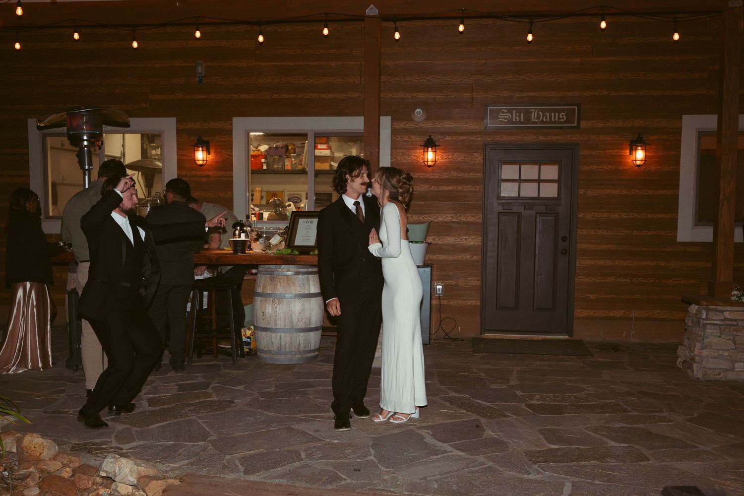 Evening wedding reception at rustic venue with string lights and wooden beams.