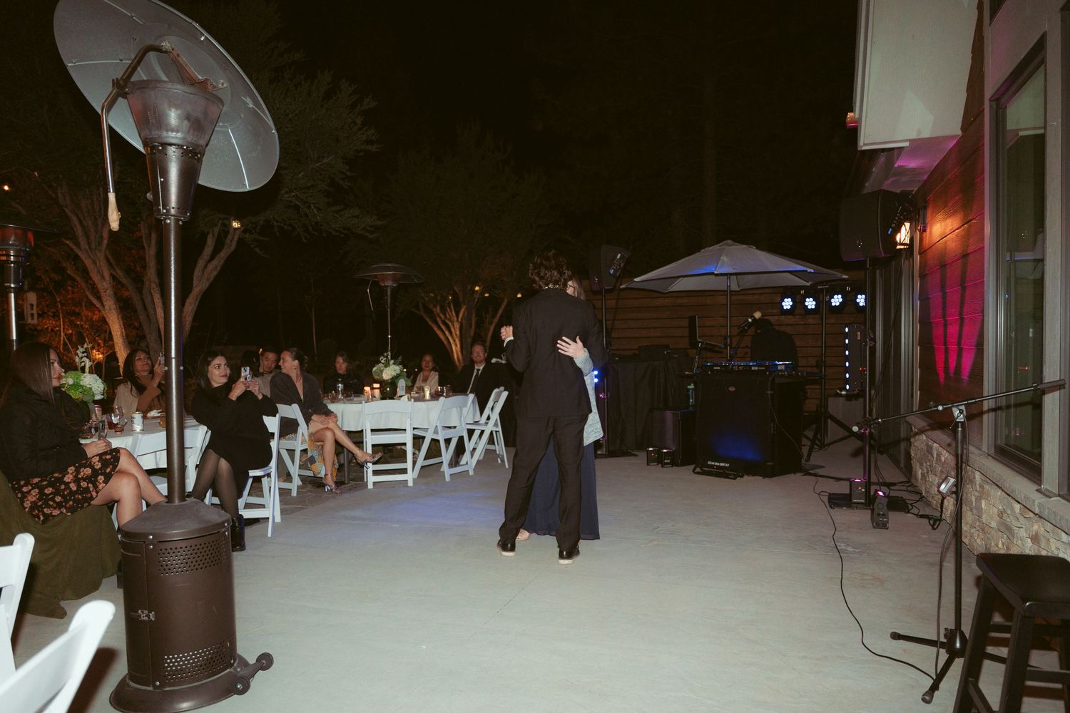 Couple dancing on an outdoor patio at night with white folding chairs and umbrellas in the background.