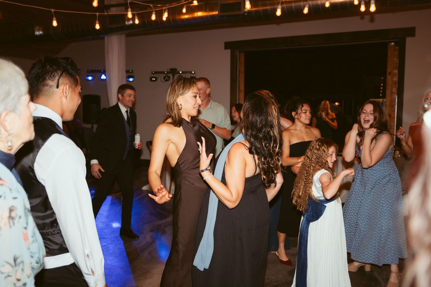 Wedding reception dance floor filled with guests under warm string lights.