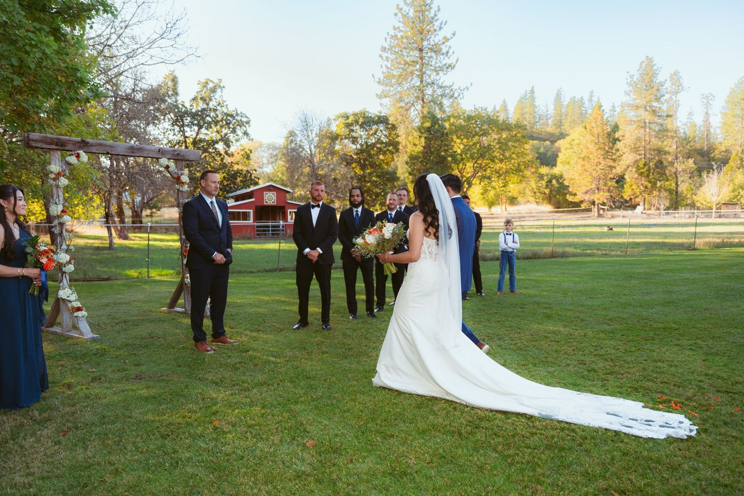 Wedding ceremony procession on grass with long white train trailing behind.