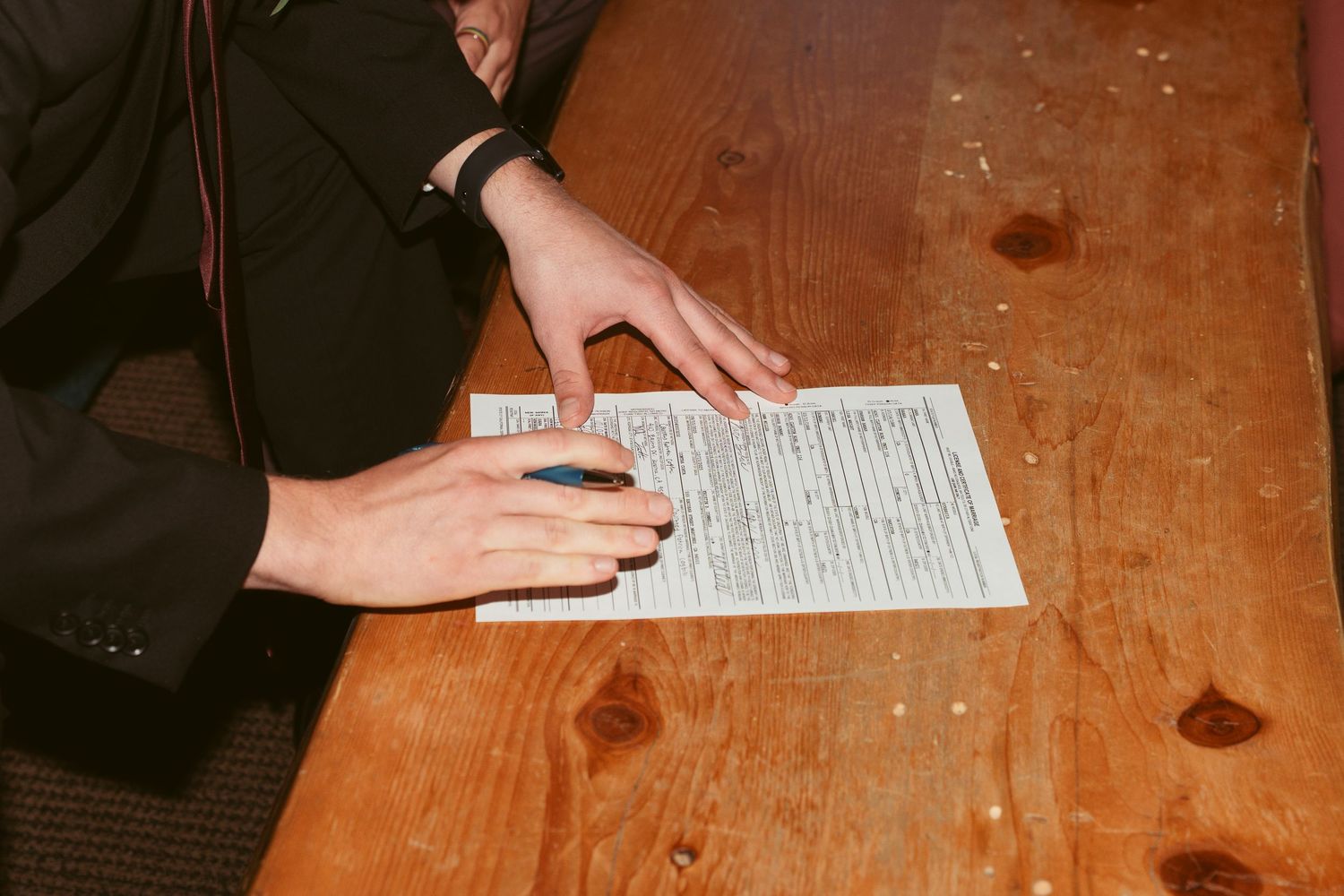 Close-up of hands signing marriage documents on rustic wooden table.