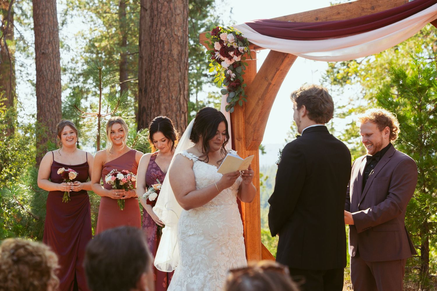 Outdoor wedding celebration under tall pine trees with rustic wooden details.