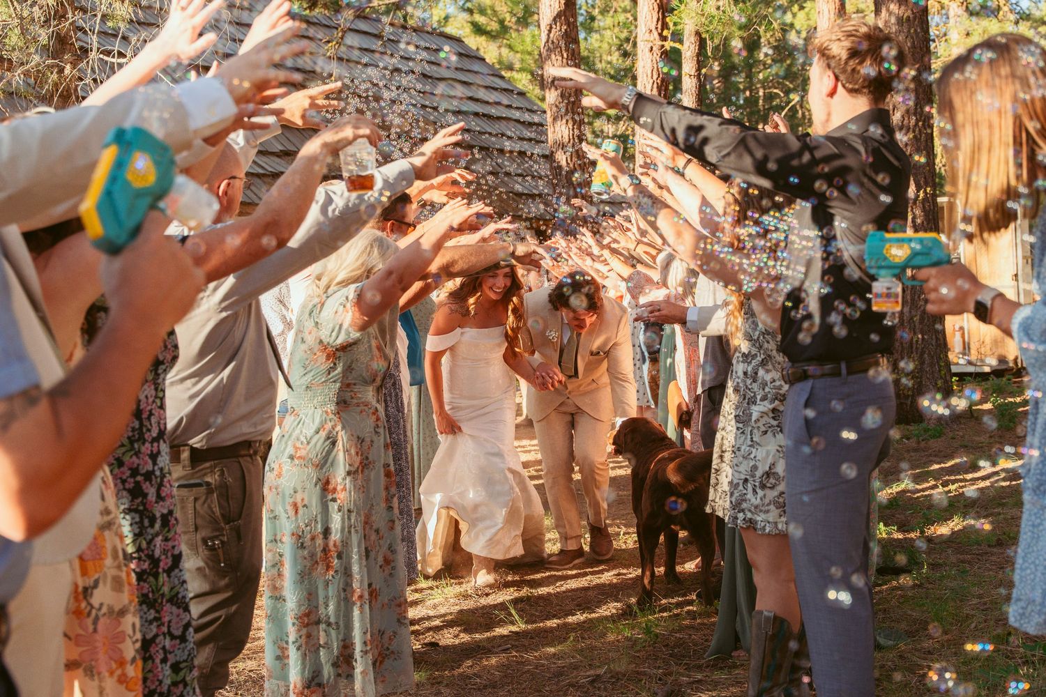 Wedding guests forming tunnel of raised arms for celebration exit in forest setting.