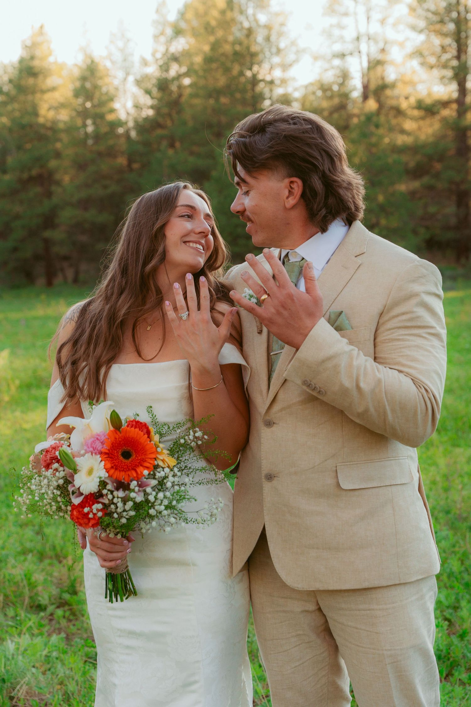 A romantic wedding couple shares intimate moments in a field with pine trees at sunset.