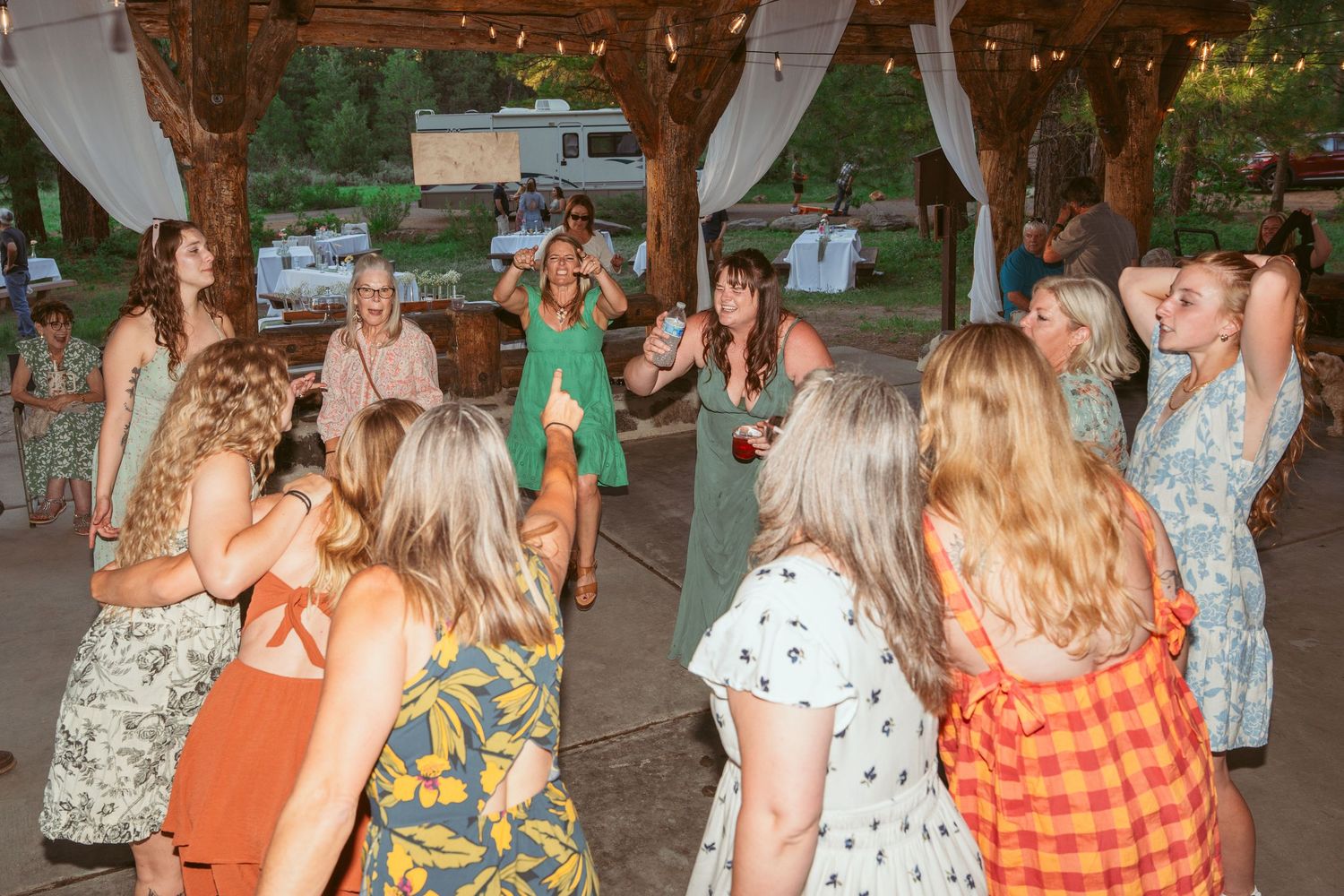 Guests in colorful summer attire dancing at an outdoor wedding reception.