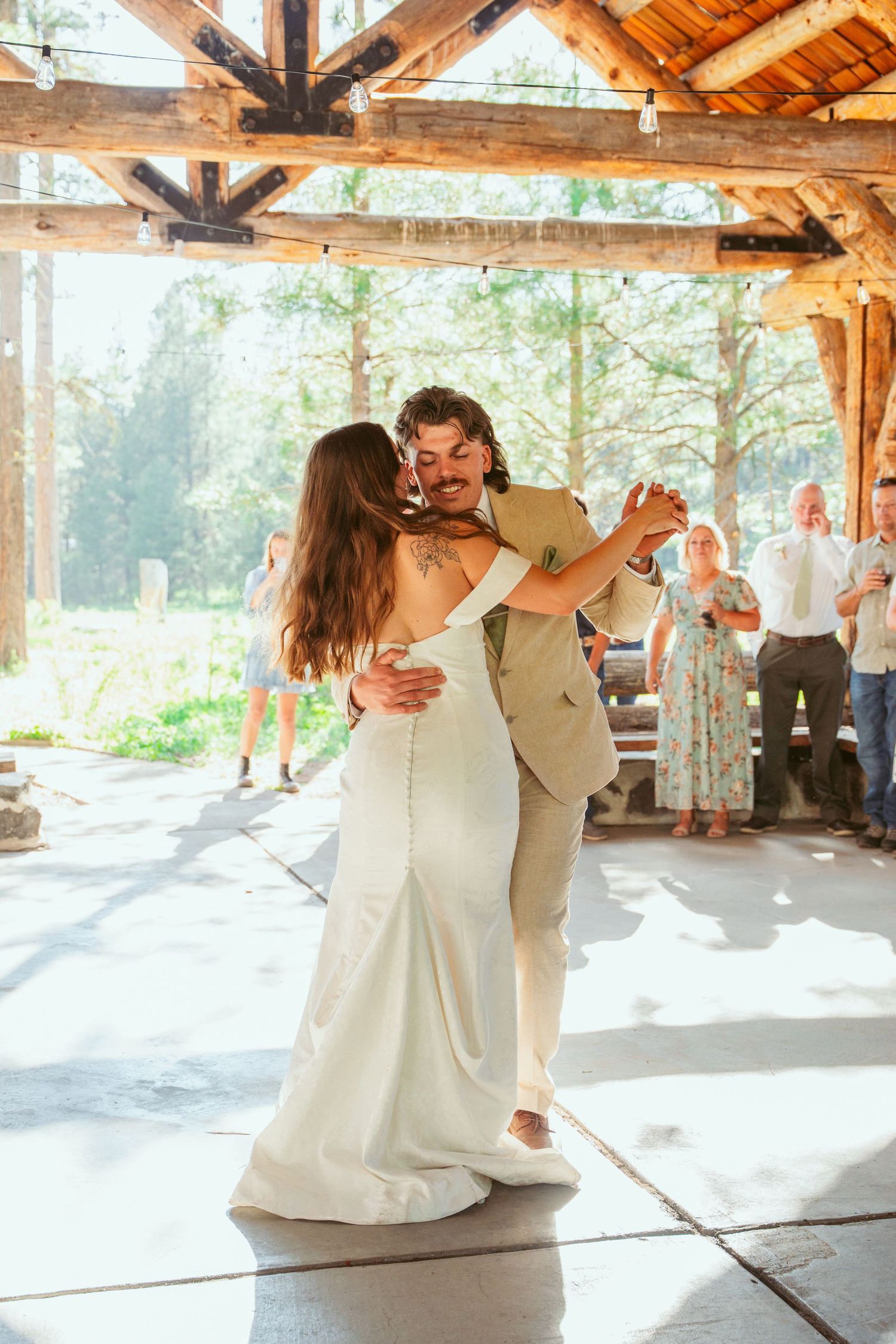 Wedding couple performs elegant dance move in rustic outdoor venue with wooden beams.
