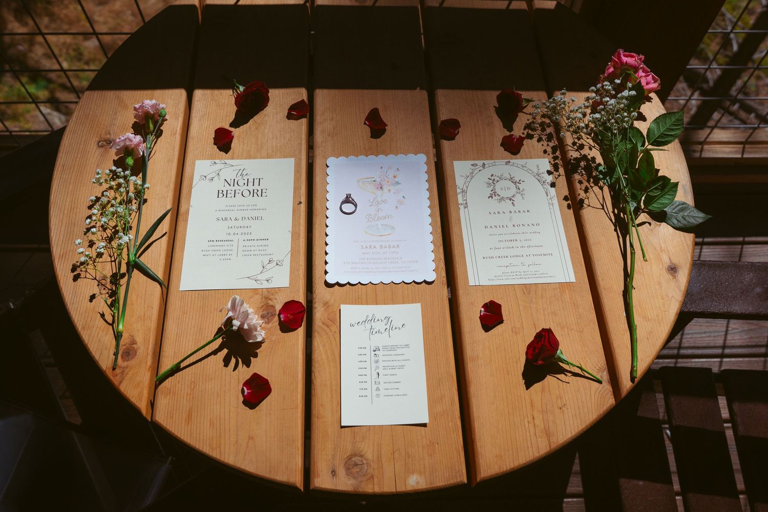 Wedding invitation cards and red roses laid out on rustic wooden table.