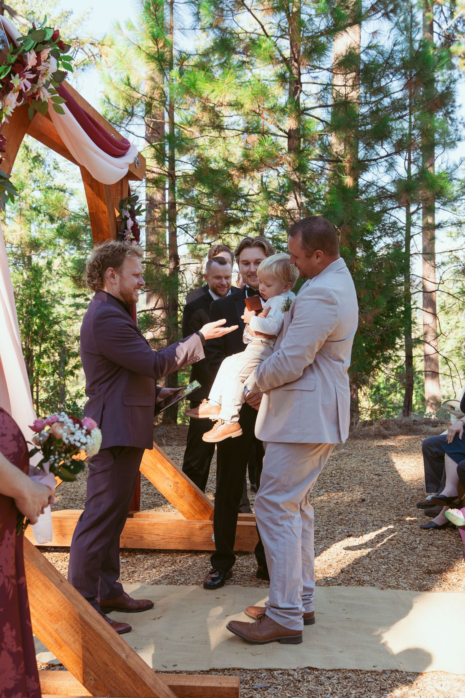 Joyful embraces between wedding party members during outdoor forest celebration.