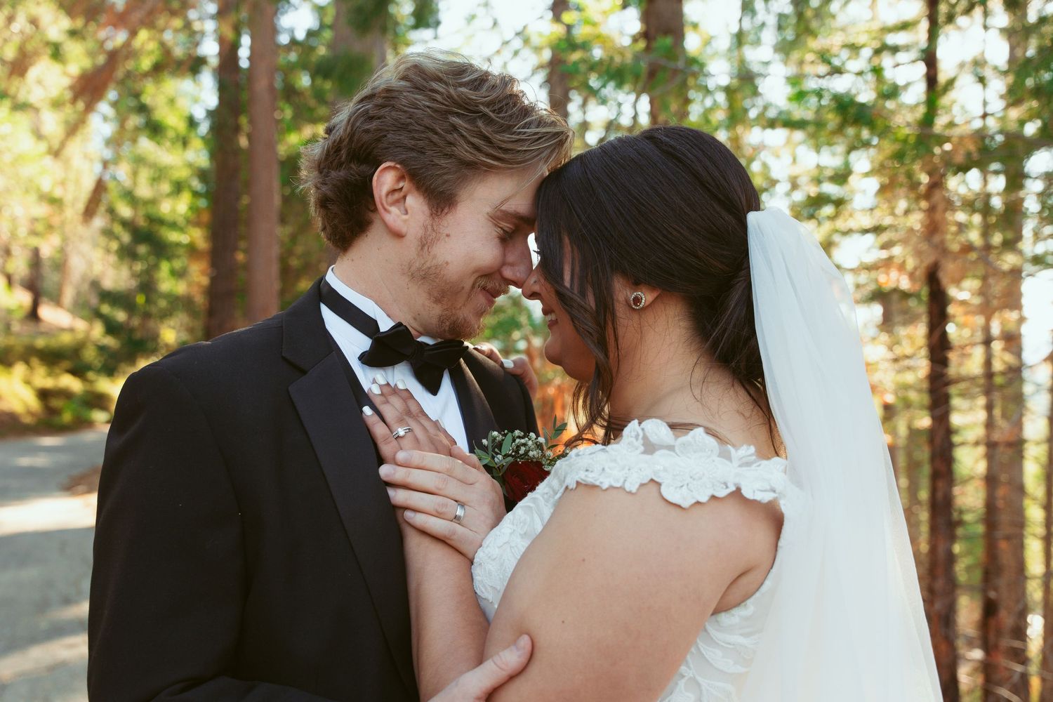 An intimate portrait of newlyweds sharing a tender moment in dappled forest lighting.