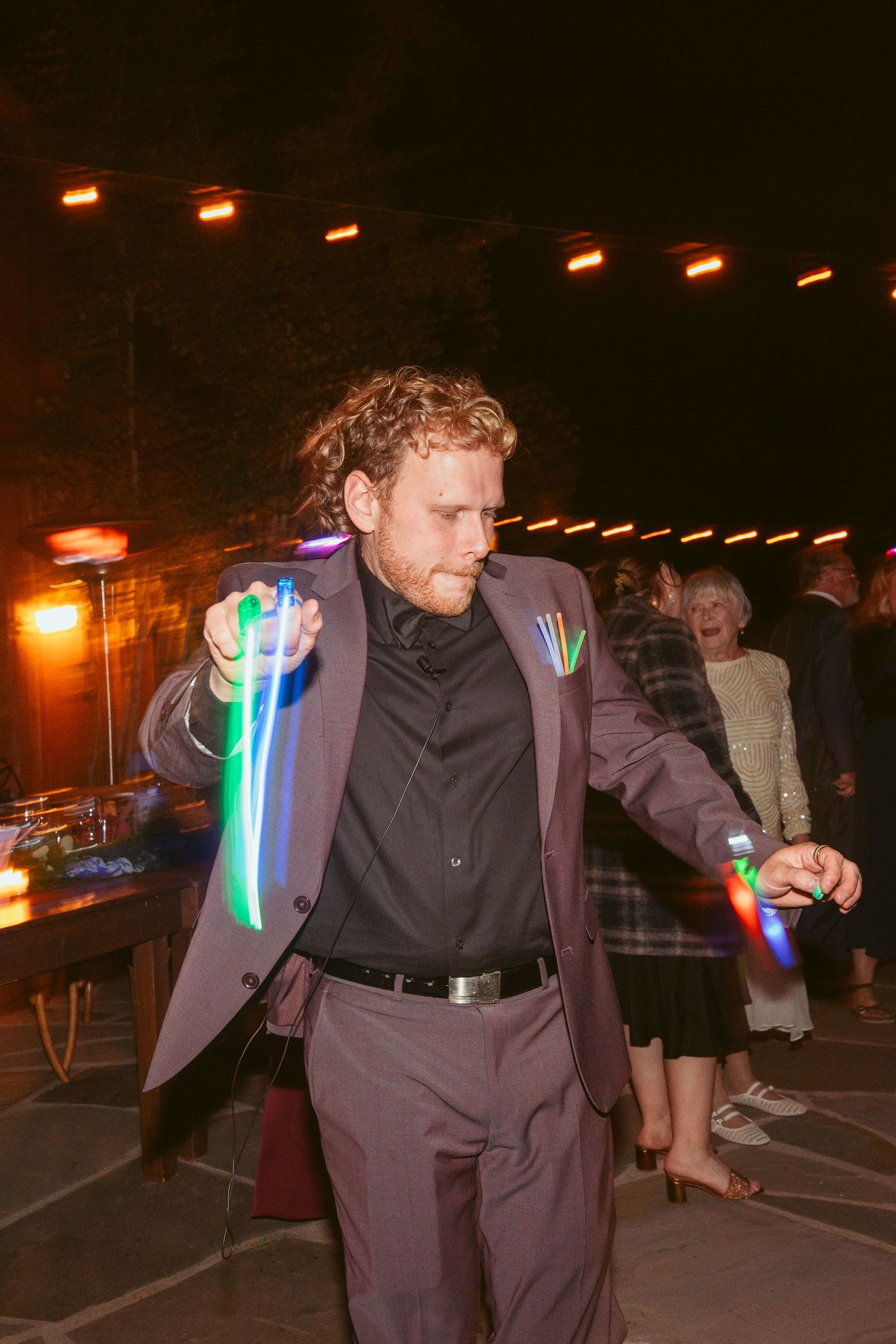 Wedding guests dance with colorful light-up glow sticks at an evening outdoor reception.