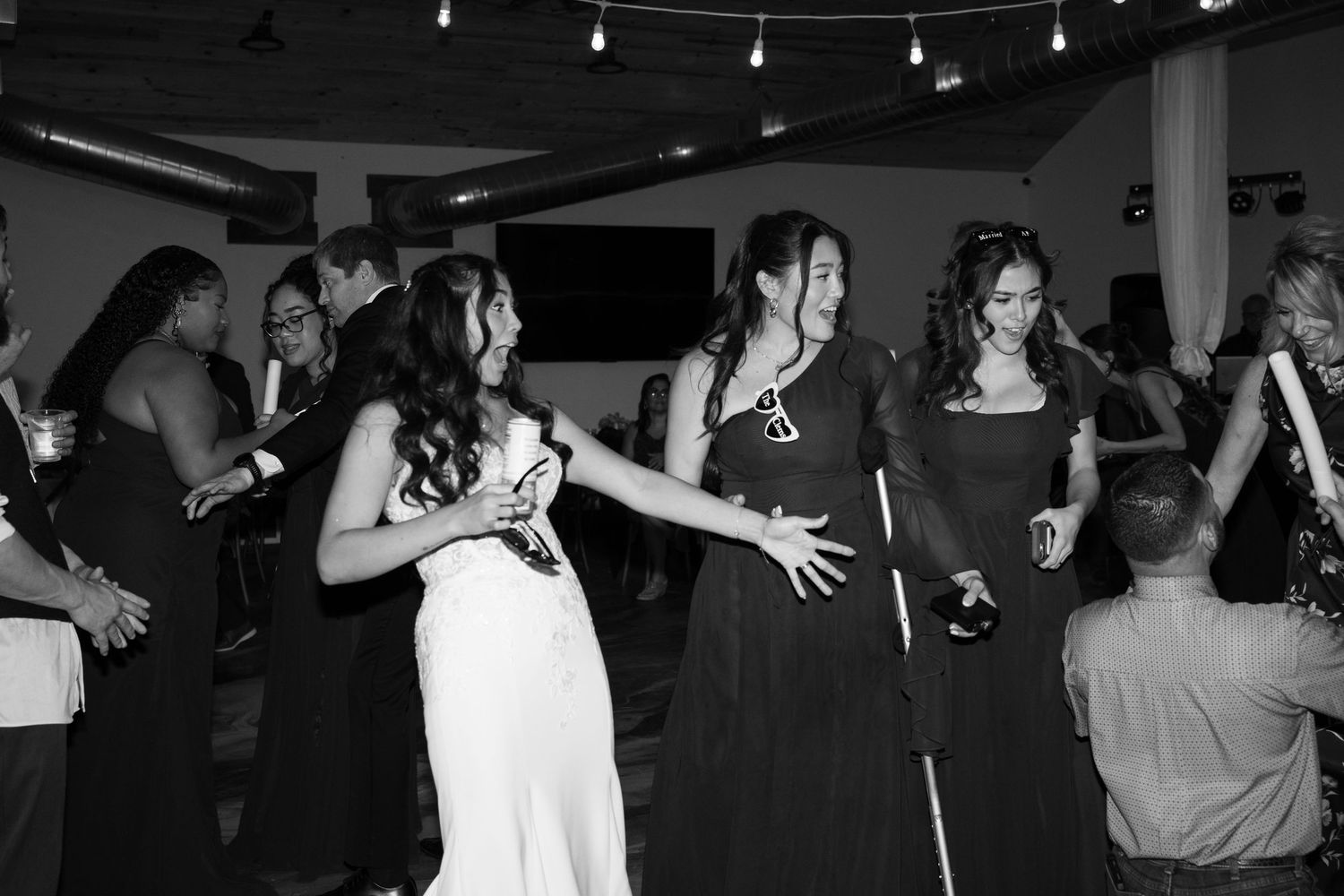 Wedding guests dancing together on a dimly lit dance floor during an evening reception celebration.