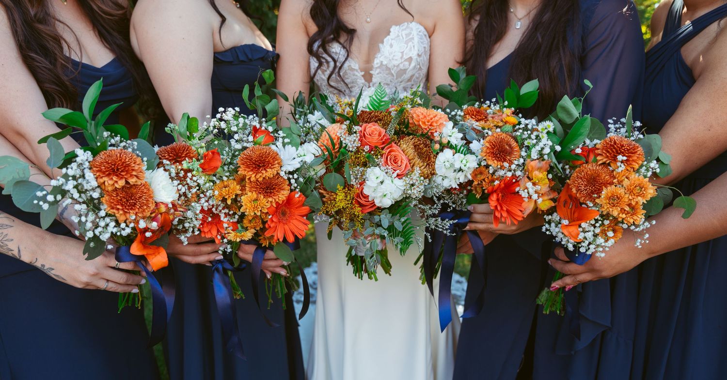 Colorful orange and white wedding bouquets displayed in a row against navy blue dresses.