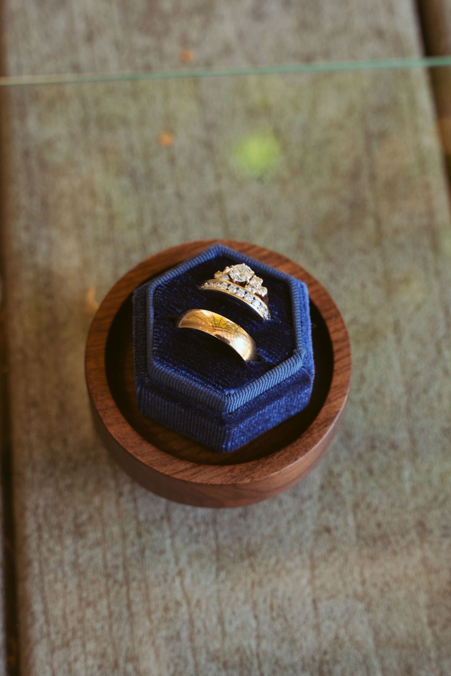 Wedding rings nestled in navy blue hexagonal box on wooden surface.