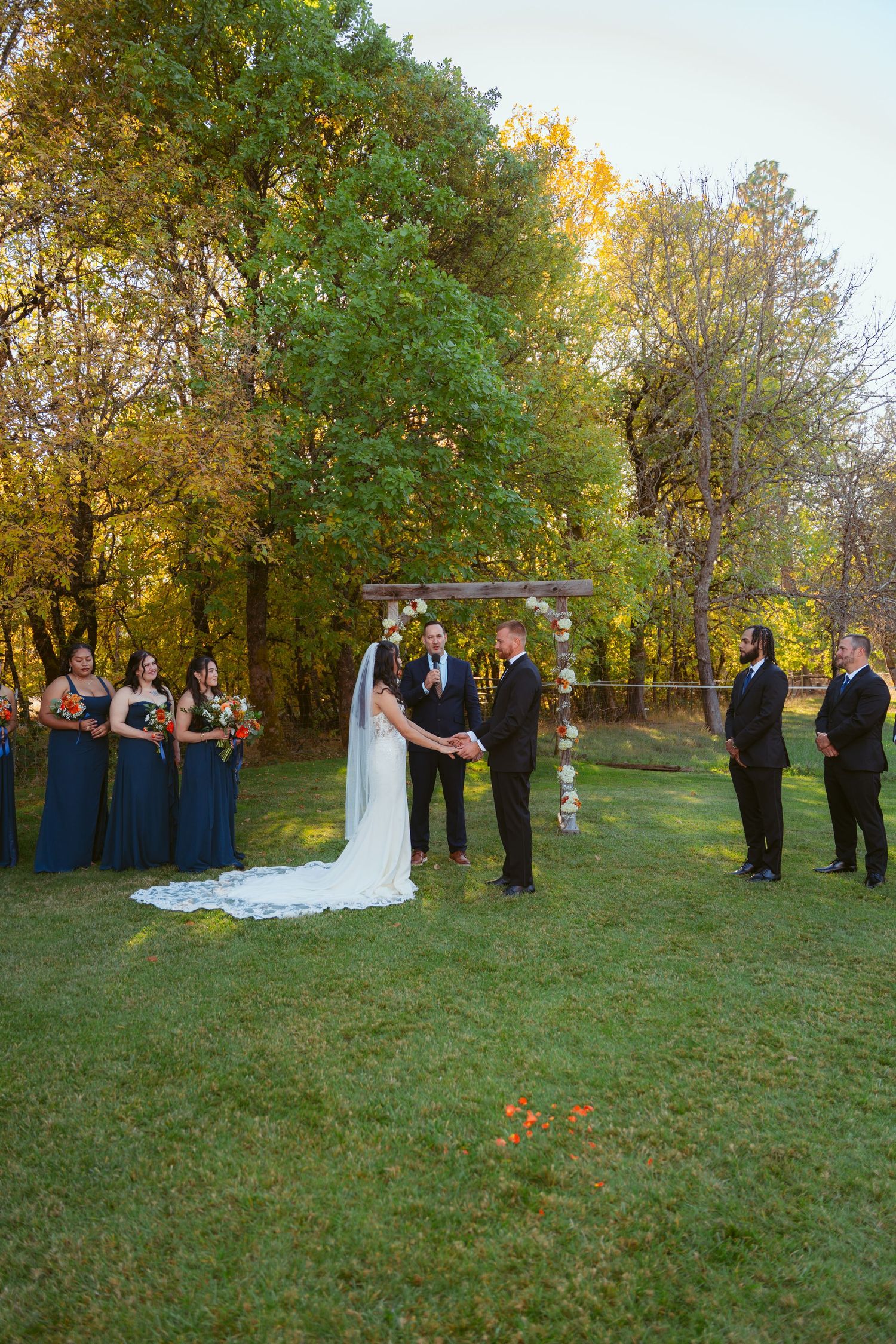 Outdoor autumn wedding ceremony with decorated arch and bridal party in navy blue.