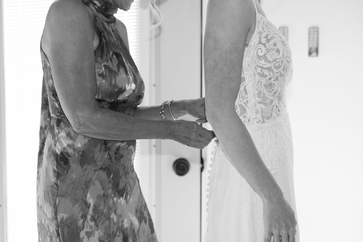 Two people in a bright room, one wearing a floral dress helping with wedding preparations.