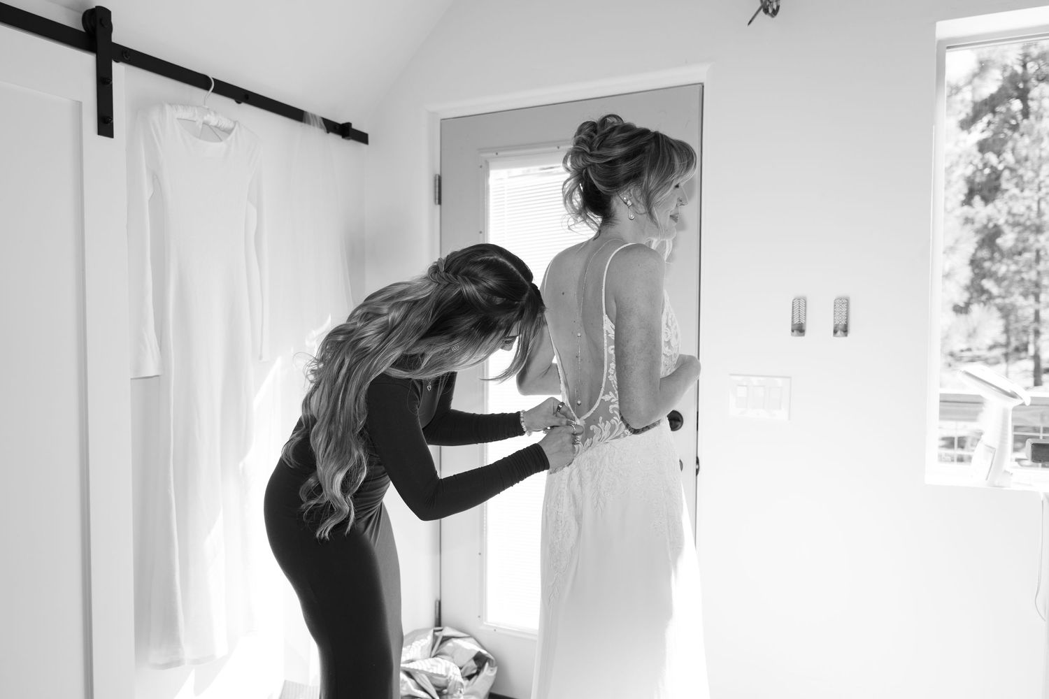 Black and white images showing someone helping with wedding dress preparations in a bright room.