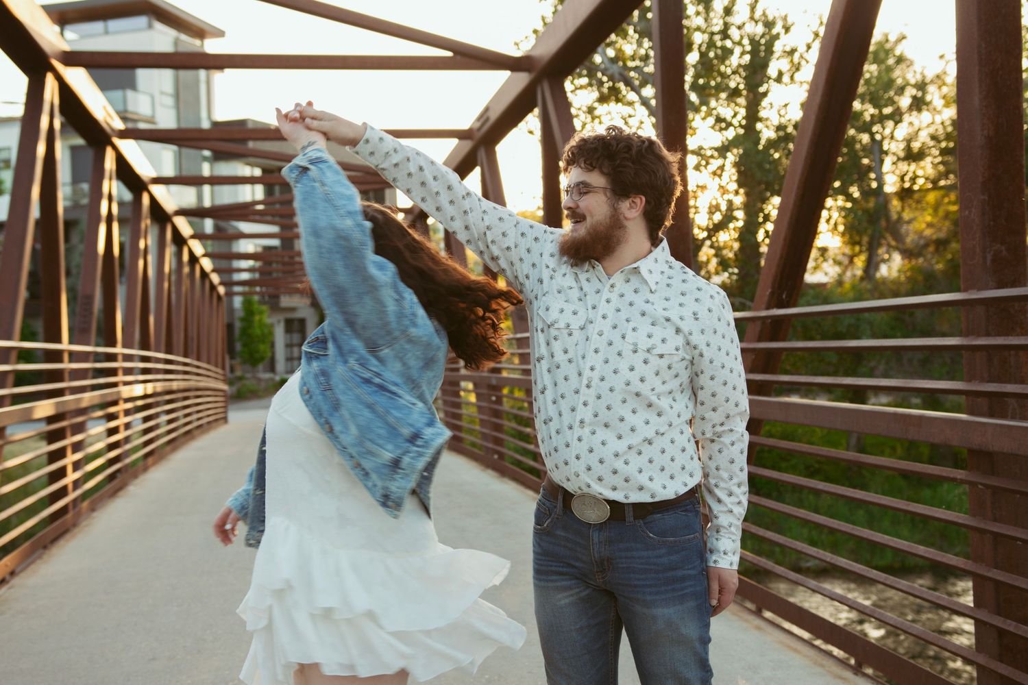 Dancing couple twirls together on a rustic bridge at sunset.