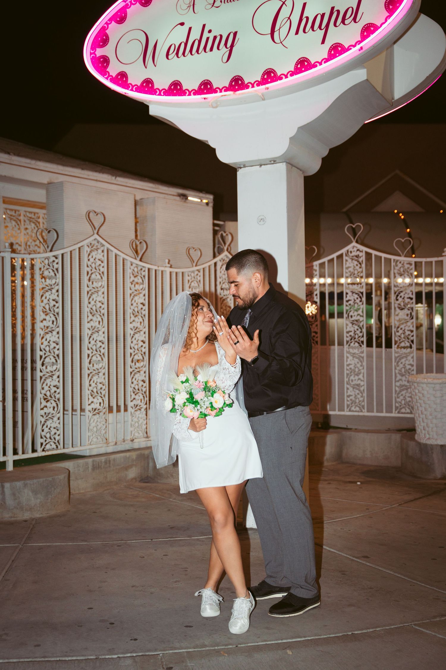 A romantic scene unfolds beneath a pink wedding chapel sign with hearts.