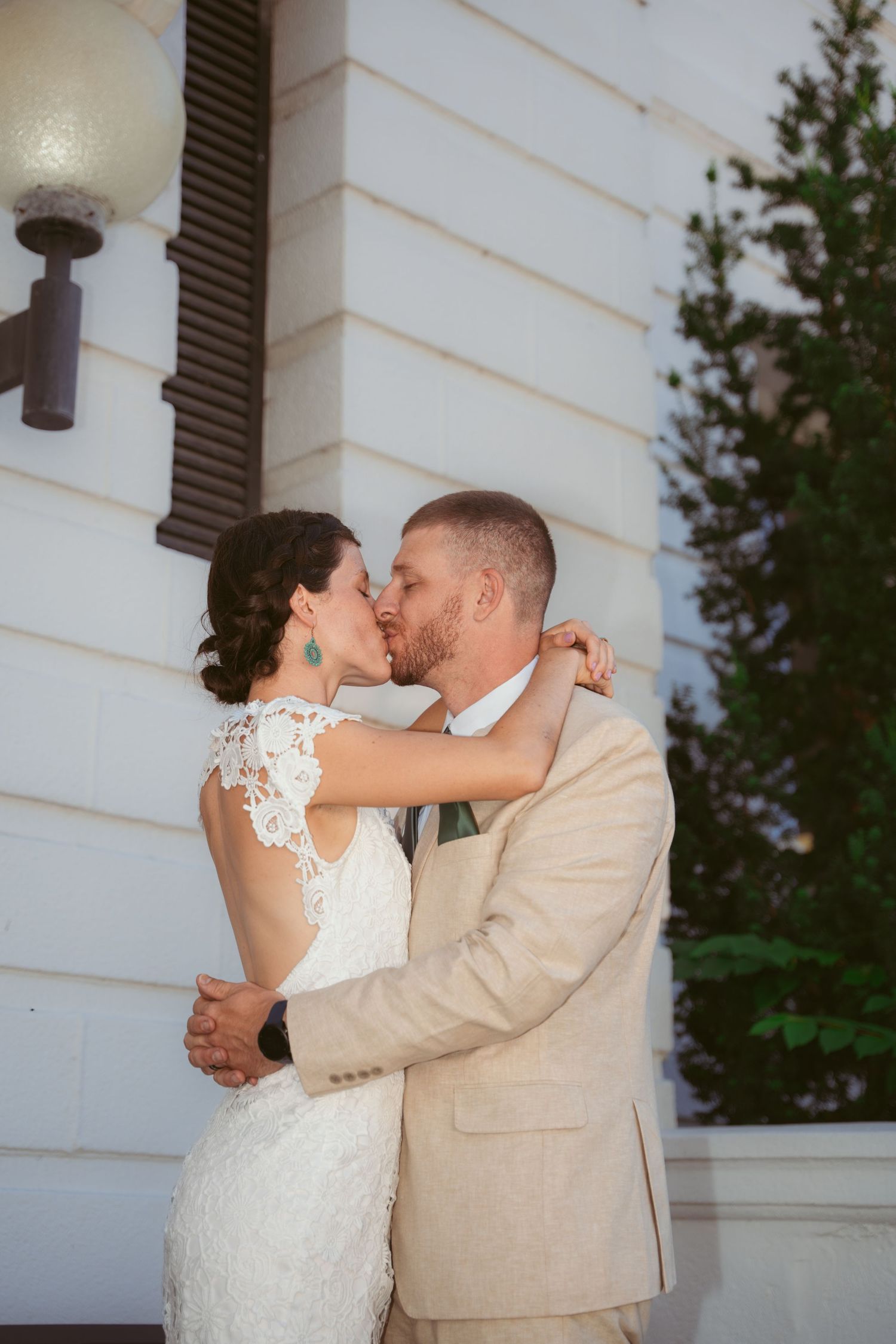 Romantic wedding couple sharing intimate moment against white building exterior.