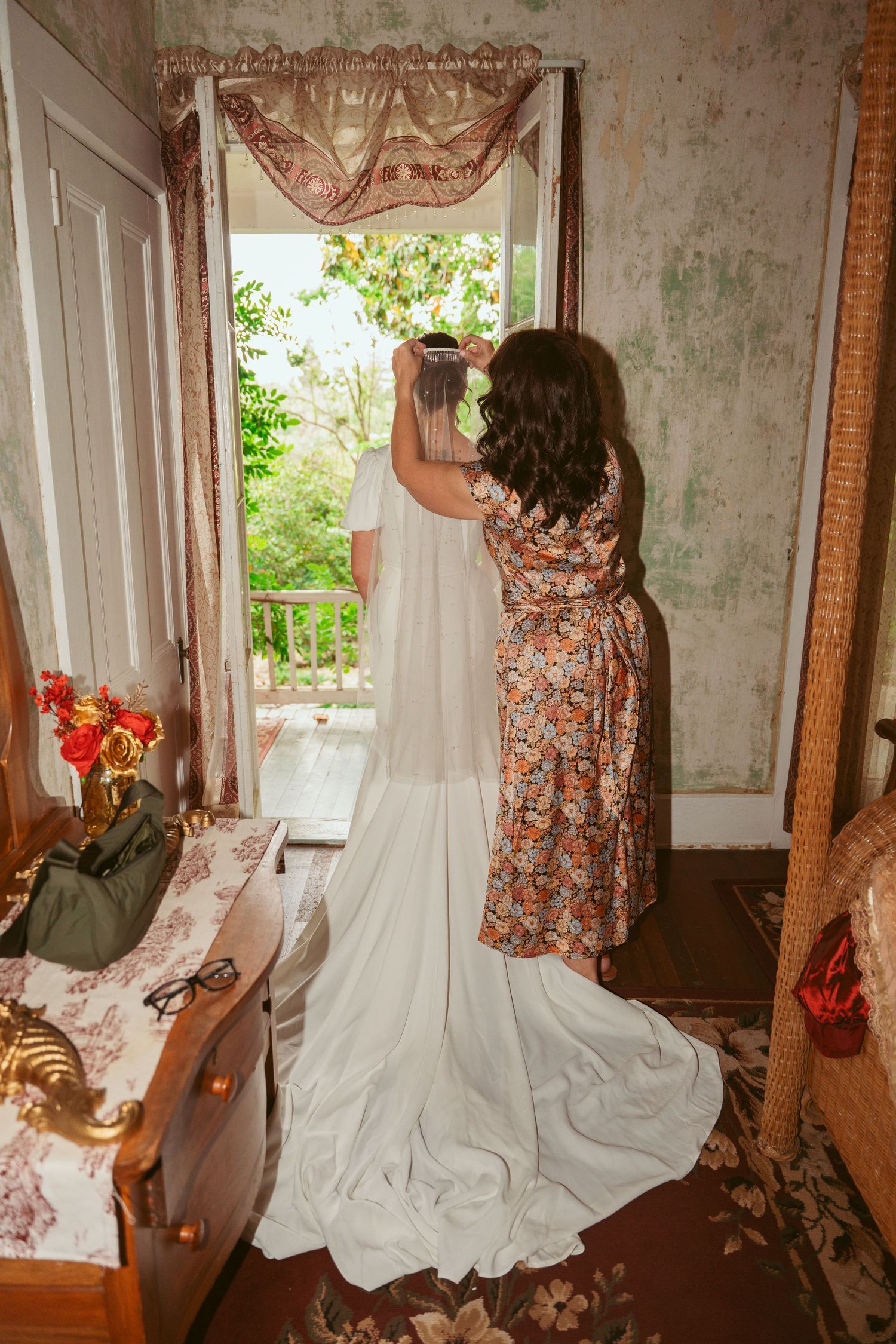 Long white wedding dress train being arranged near a window in a vintage-style room.