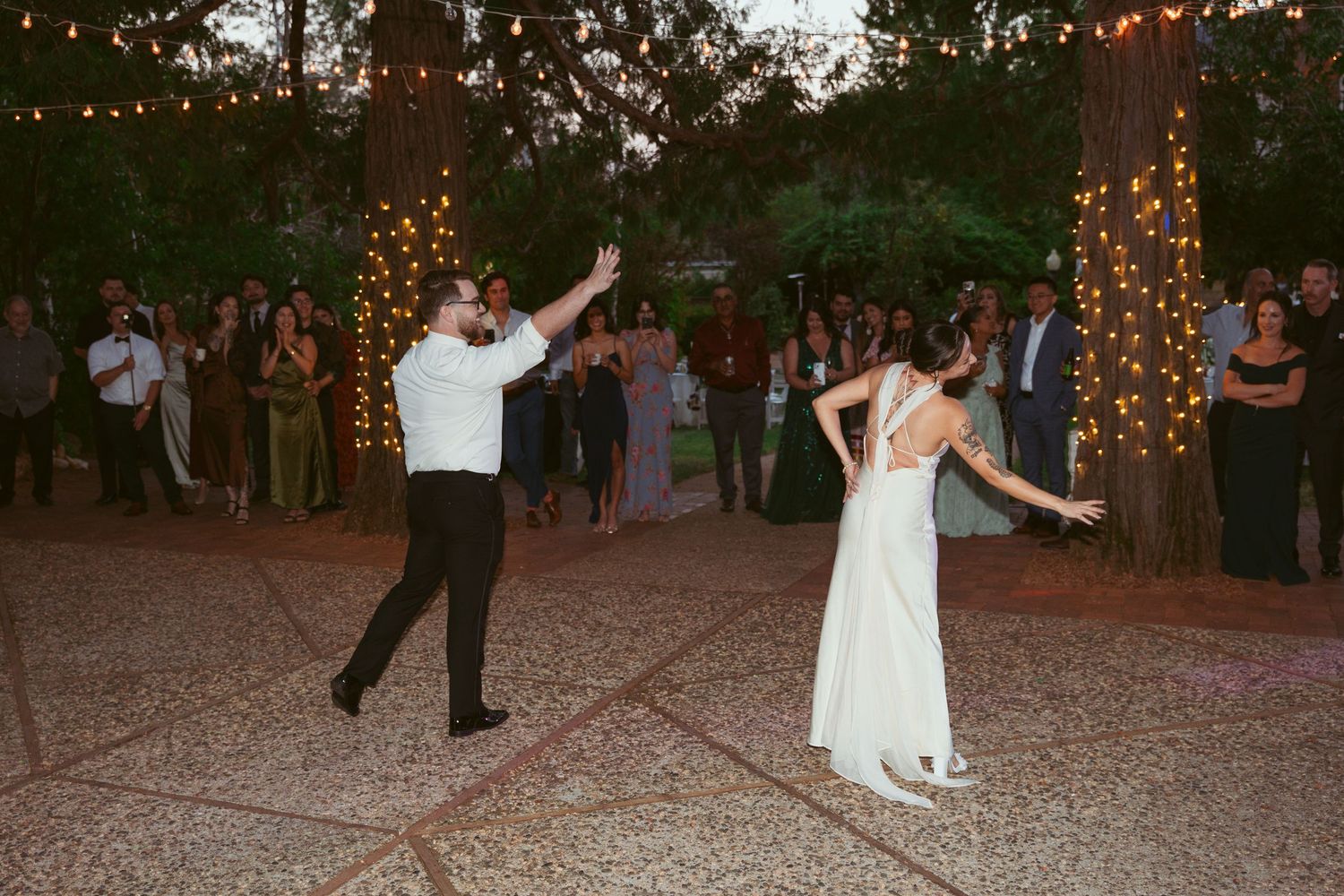 A couple performs a choreographed dance routine at their outdoor wedding reception.