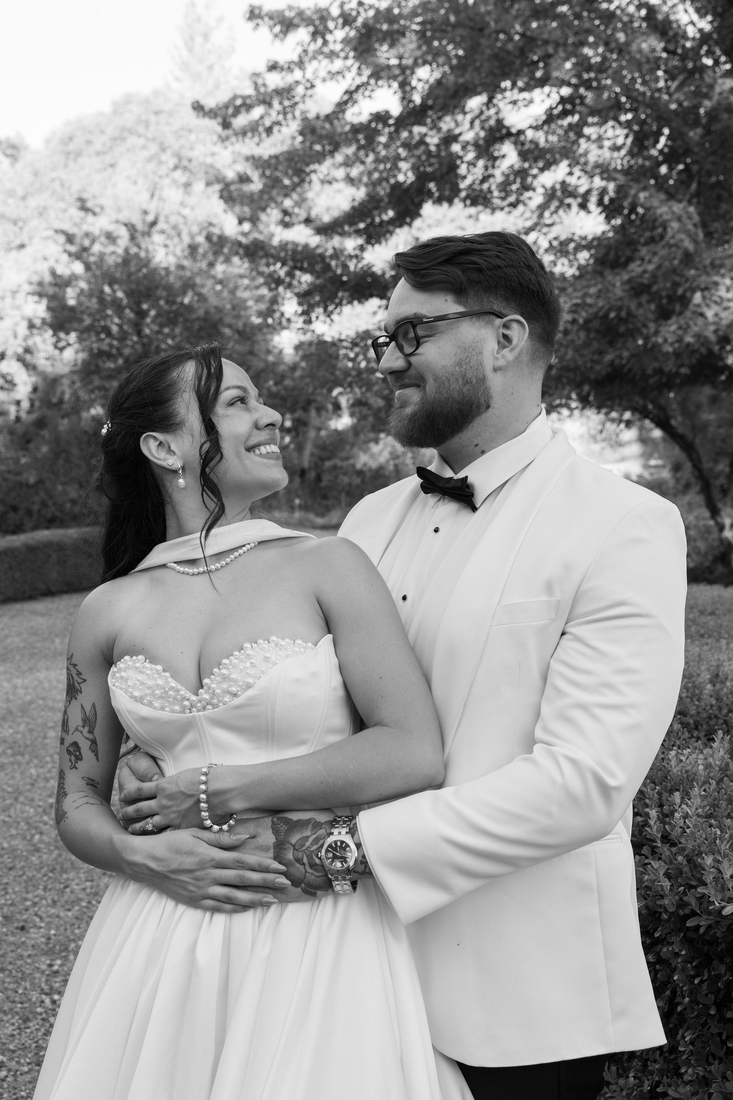 A romantic black and white portrait of a newlywed couple embracing outdoors, with the bride in a strapless gown.