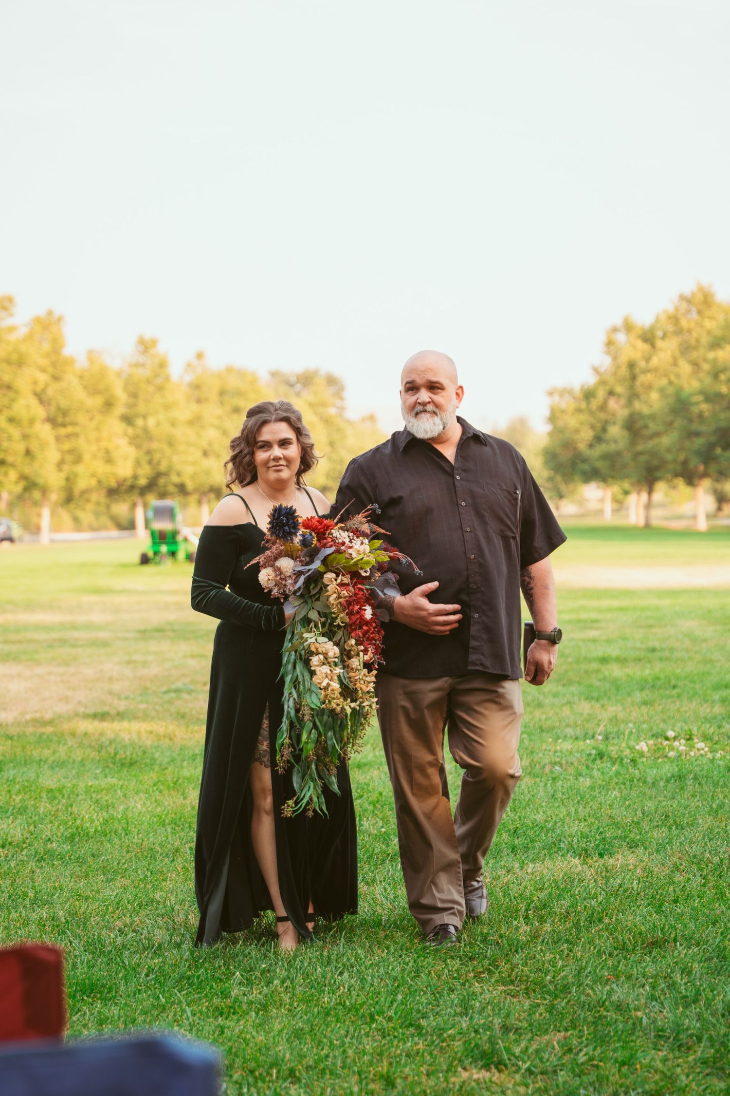 A couple stands in a grassy field during golden hour sharing an intimate moment with autumn trees in the background.