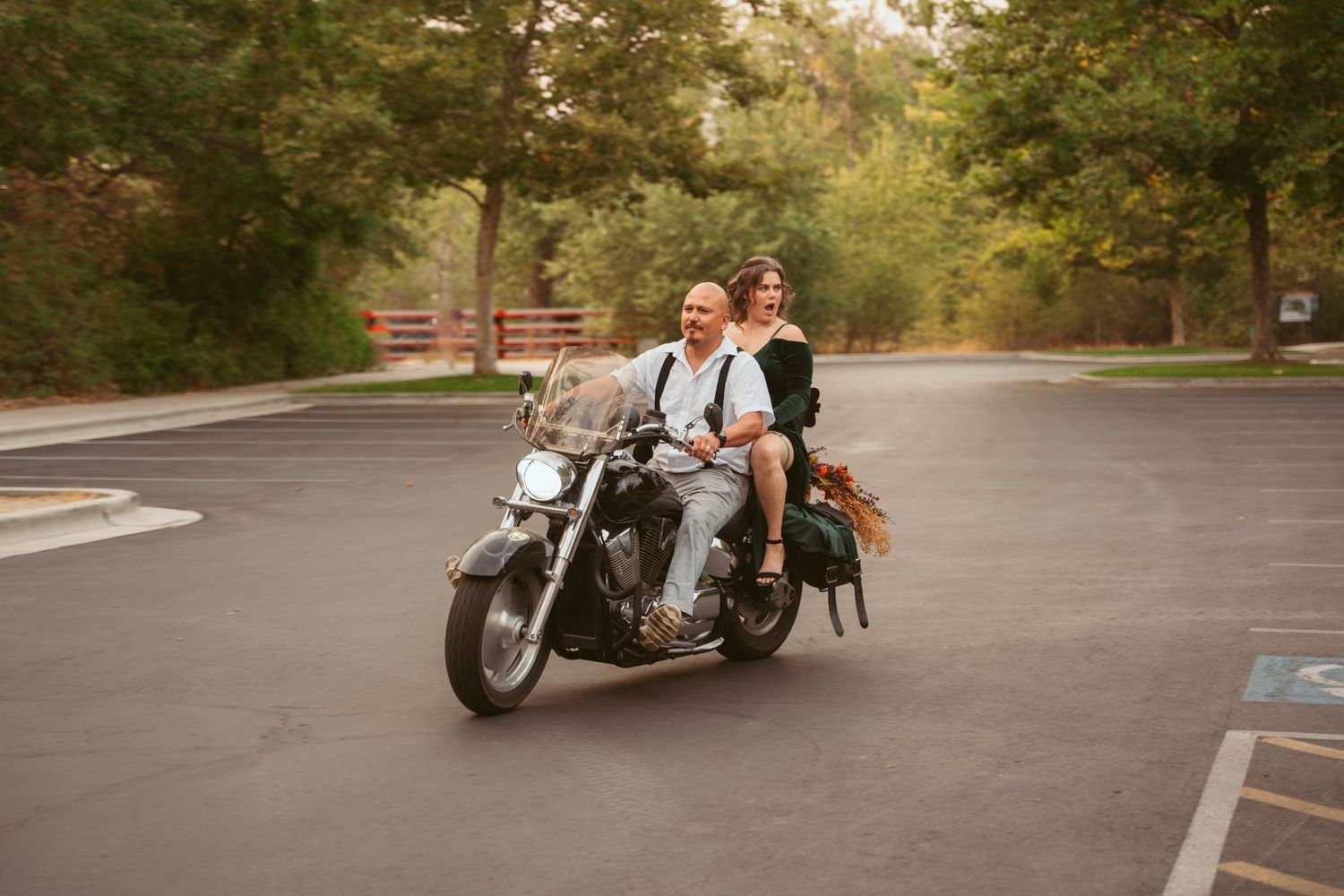 A couple rides together on a motorcycle in a parking lot during golden hour.