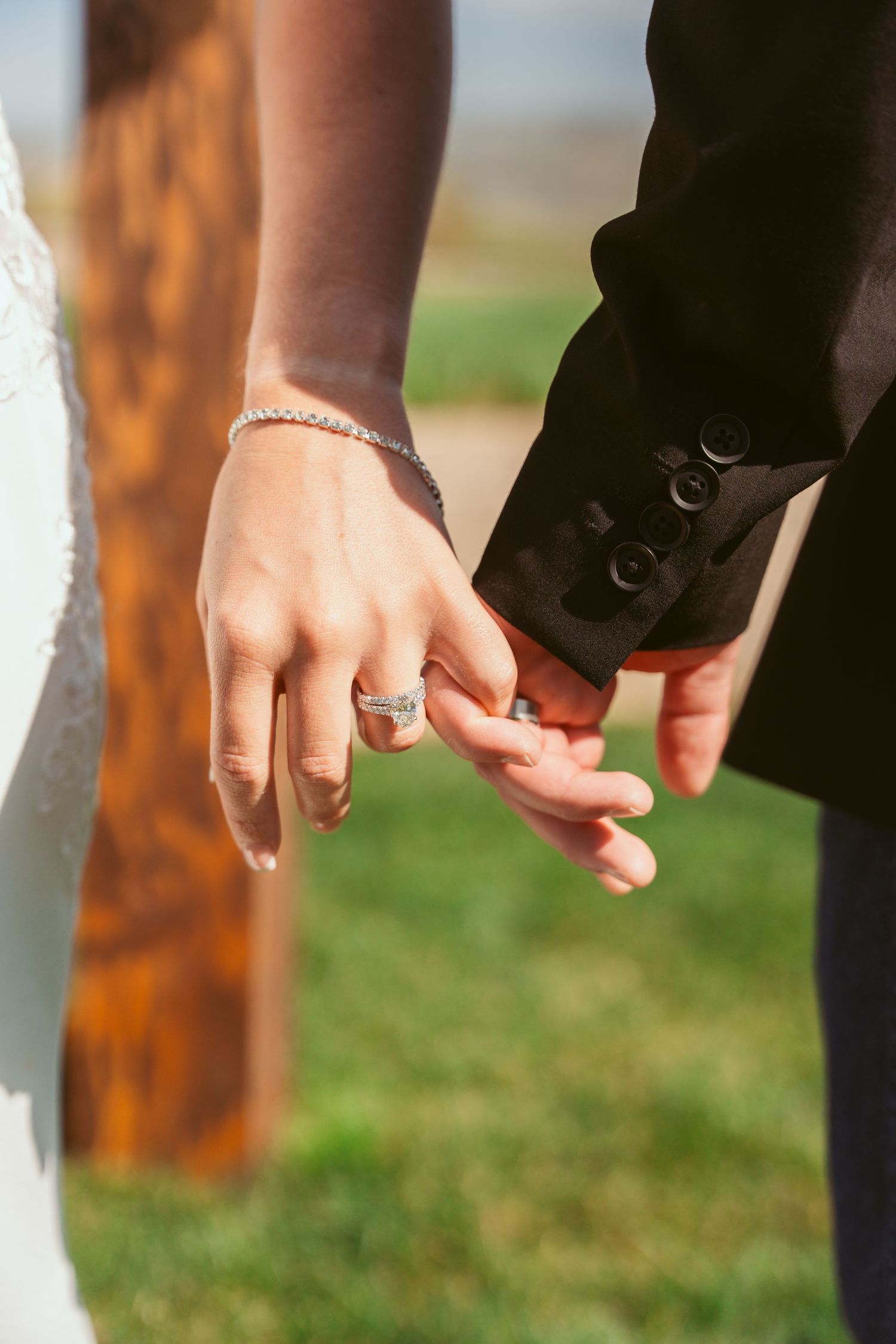 Close-up of hands showing wedding rings against a grassy background.