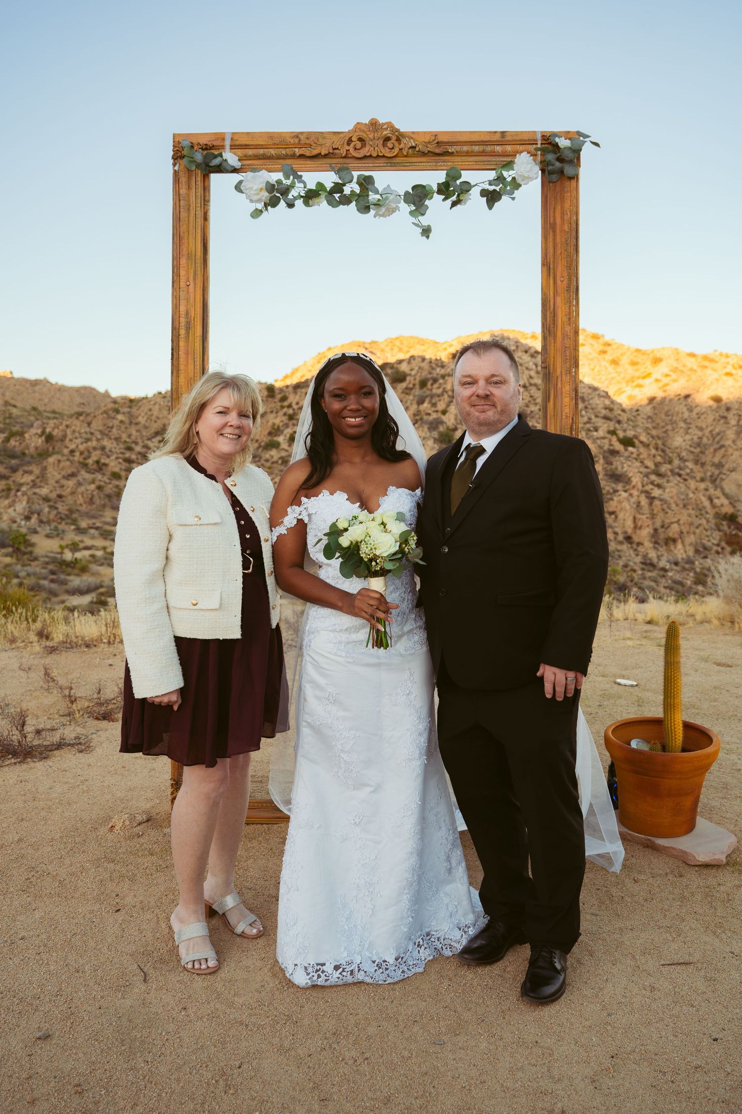 Wedding party poses under a wooden arch in a desert setting with mountains behind them.