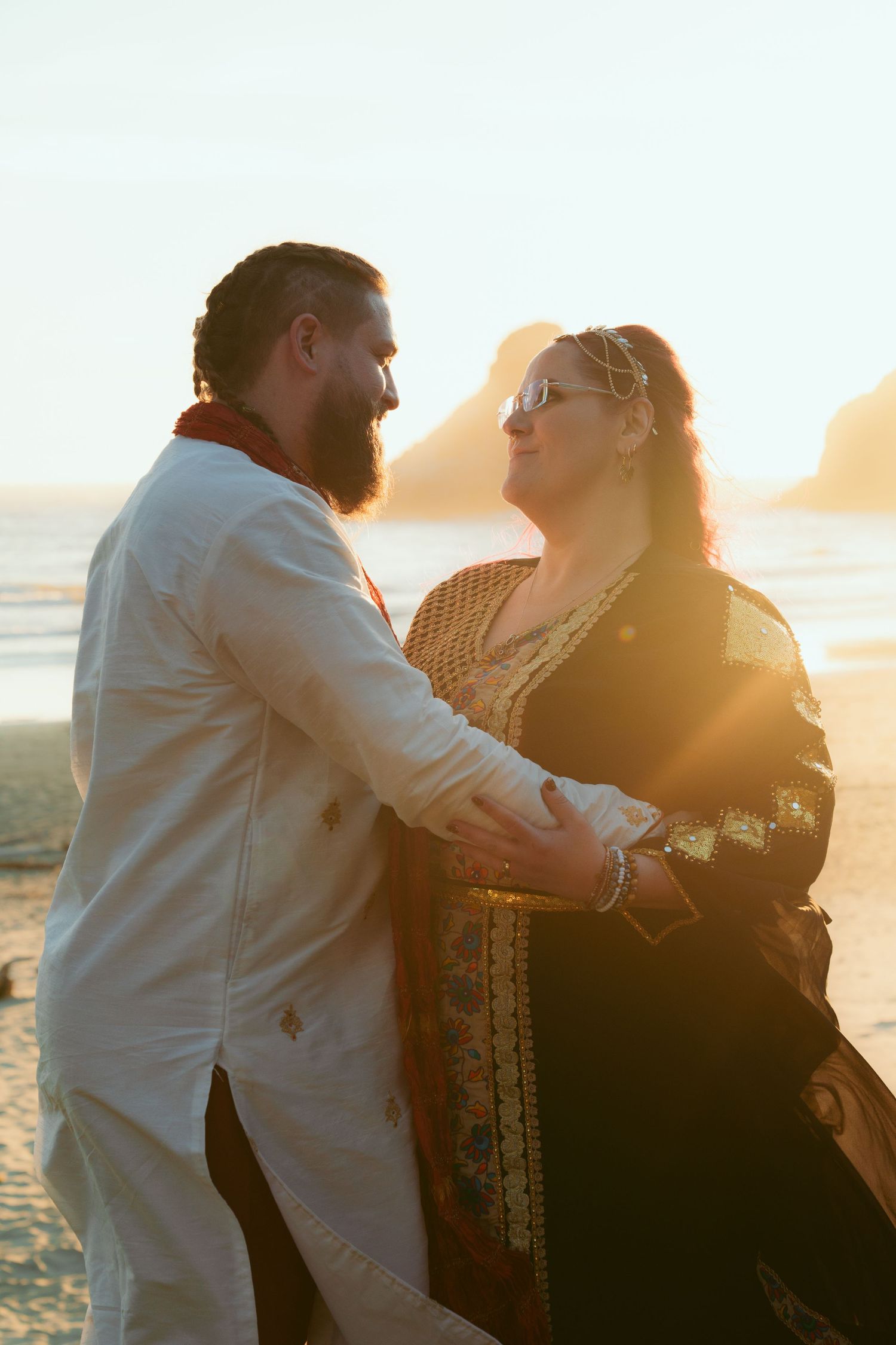 Couple dances together on beach during sunset with dramatic coastal backdrop.