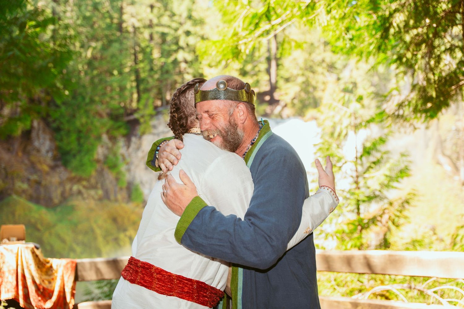 A romantic outdoor wedding ceremony takes place in a sunlit forest clearing.