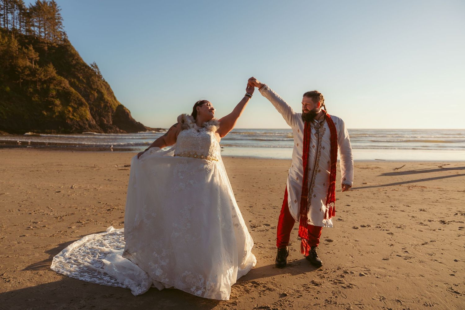 Two people in formal attire dance and spin on a beach with dramatic coastal cliffs in the background.