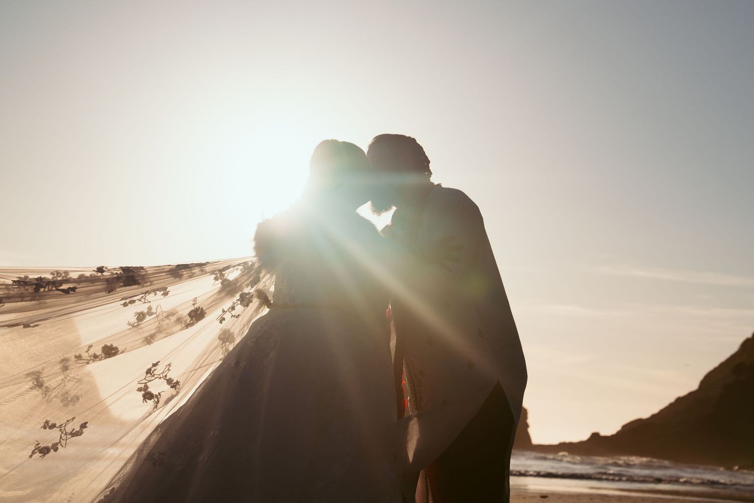 Silhouettes of a couple embracing during sunset at their beach wedding.