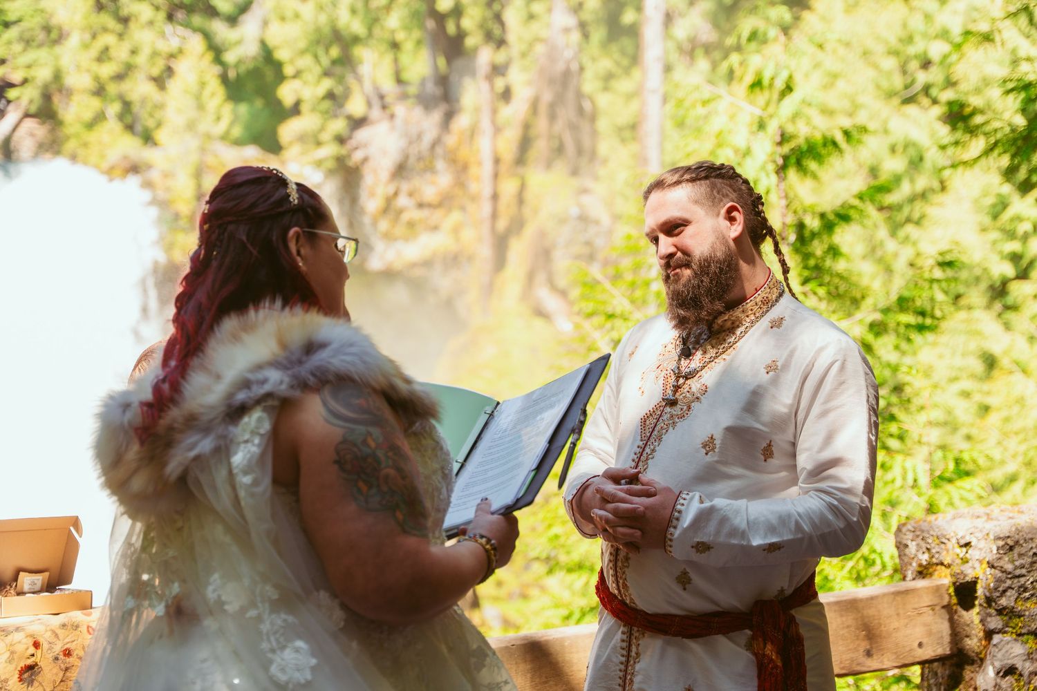 A medieval-themed outdoor wedding ceremony in a lush forest setting with guests seated on wooden benches.