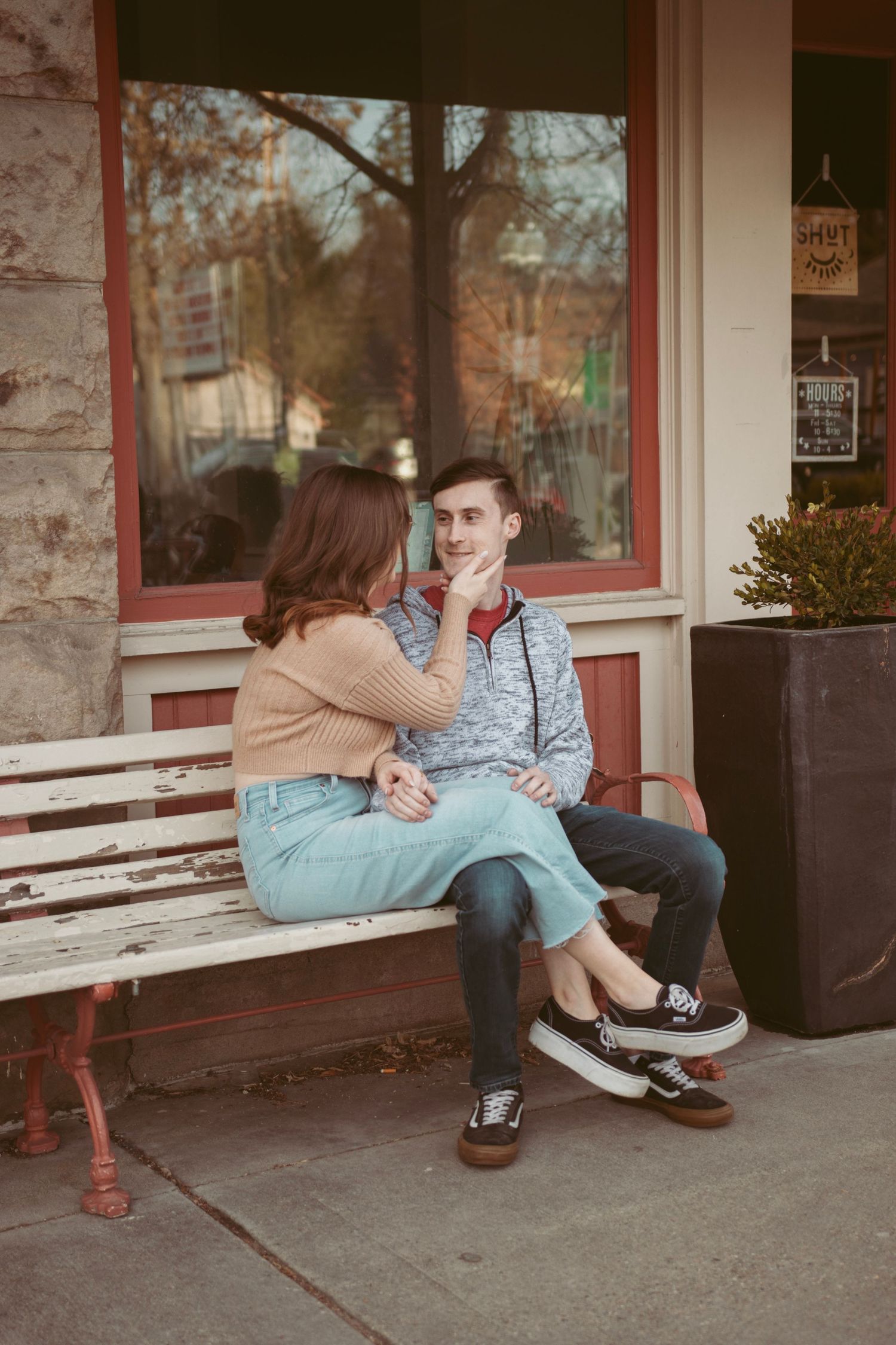 A couple shares a tender moment while sitting on a bench outside a storefront.