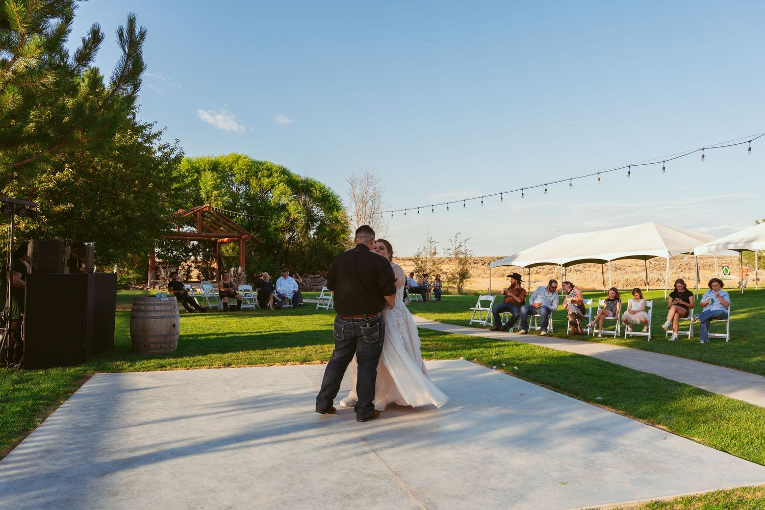 Wedding celebration on an outdoor dance floor with string lights overhead at sunset.