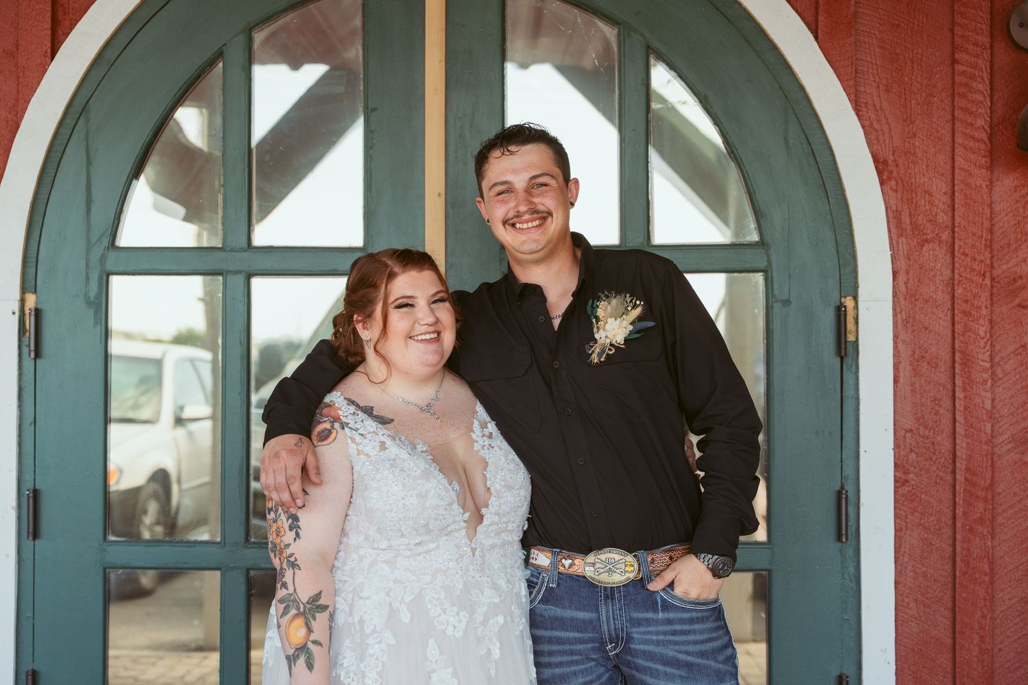 Newlyweds share a happy moment in front of teal arched doorway on red building.