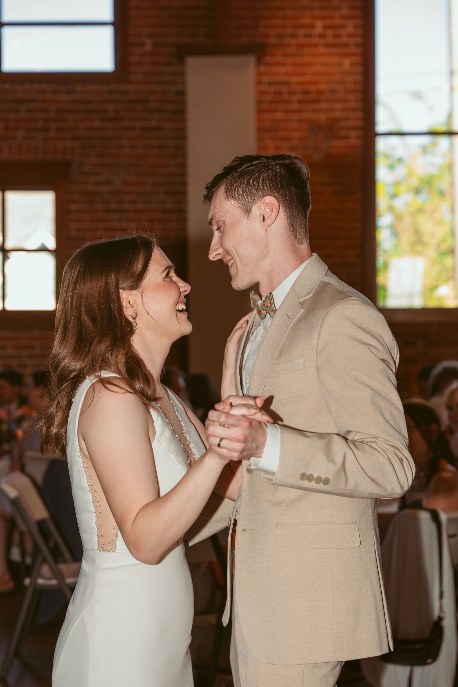Couple sharing their first dance in a rustic brick venue with natural lighting.