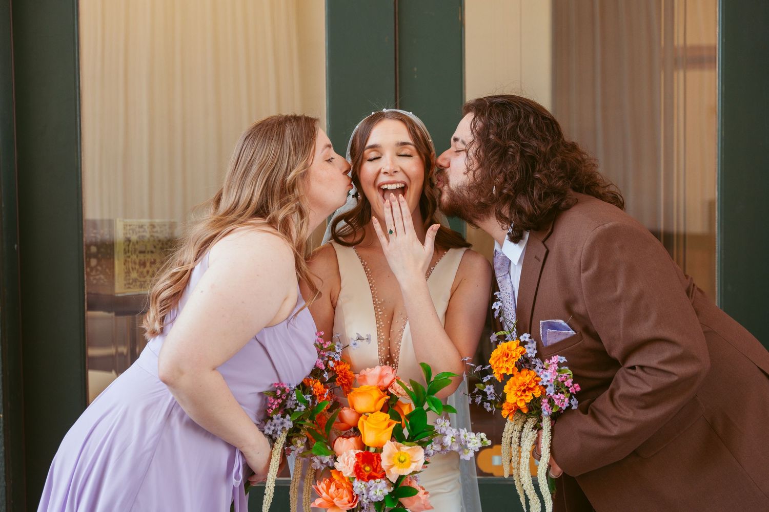 Three people share a joyful moment with laughter during wedding photos.