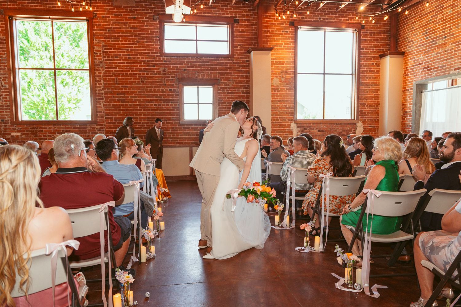 Panoramic view of wedding ceremony space with exposed brick walls and white chair seating.
